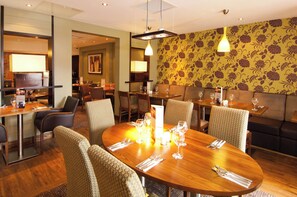 A restaurant with round tables, chairs, and a patterned wall. - Premier Inn Sunbury (Sunbury on Thames)