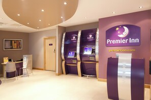 A Premier Inn reception area with check-in kiosks and a private room door. - Premier Inn Sunbury (Sunbury on Thames)