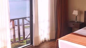 Une chambre d’hôtel avec un lit, une table de chevet, une lampe, une fenêtre avec des rideaux et une vue sur la mer.
