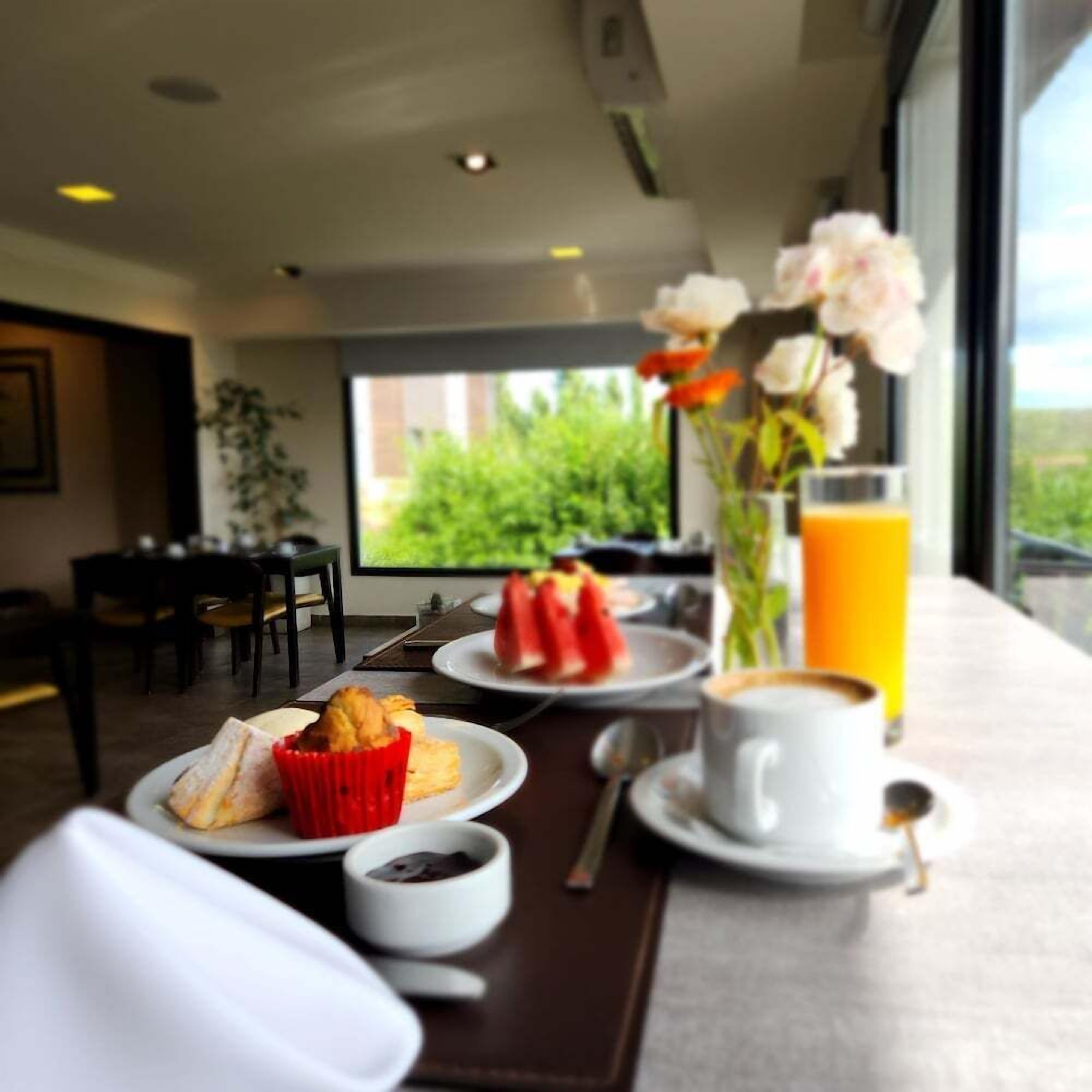 A breakfast setting with a table, plates of food, a cup of coffee, a glass of orange juice, and a vase with flowers.
