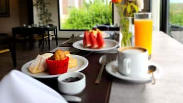 A breakfast setting with a table, plates of food, a cup of coffee, a glass of orange juice, and a vase with flowers.