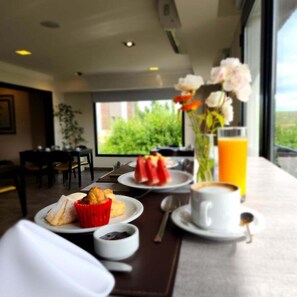 A breakfast setting with a table, plates of food, a cup of coffee, a glass of orange juice, and a vase with flowers. - Xelena Hotel and Suites (El Calafate)