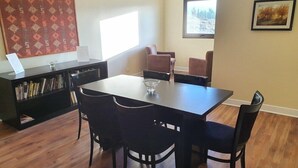 Uma área de refeições com mesa e cadeiras, uma estante de livros e uma janela com vista.