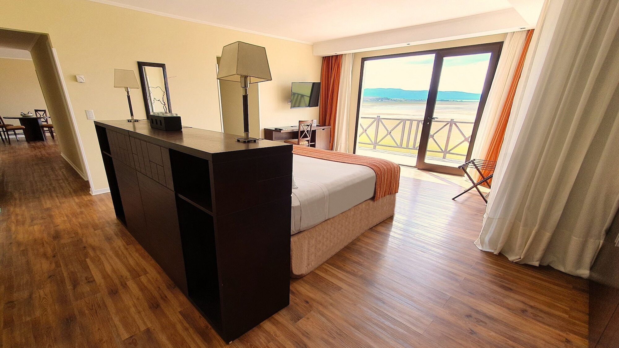 A hotel room with a bed, a desk, a TV, and a balcony with curtains.