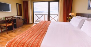 A hotel room with a bed, a desk, a chair, a television, and a view of the sea. - Xelena Hotel and Suites (El Calafate)