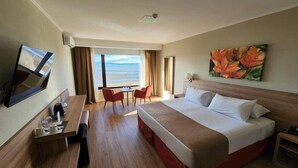 Quarto de hotel com cama, escrivaninha, cadeira, televisão e janela com vista.