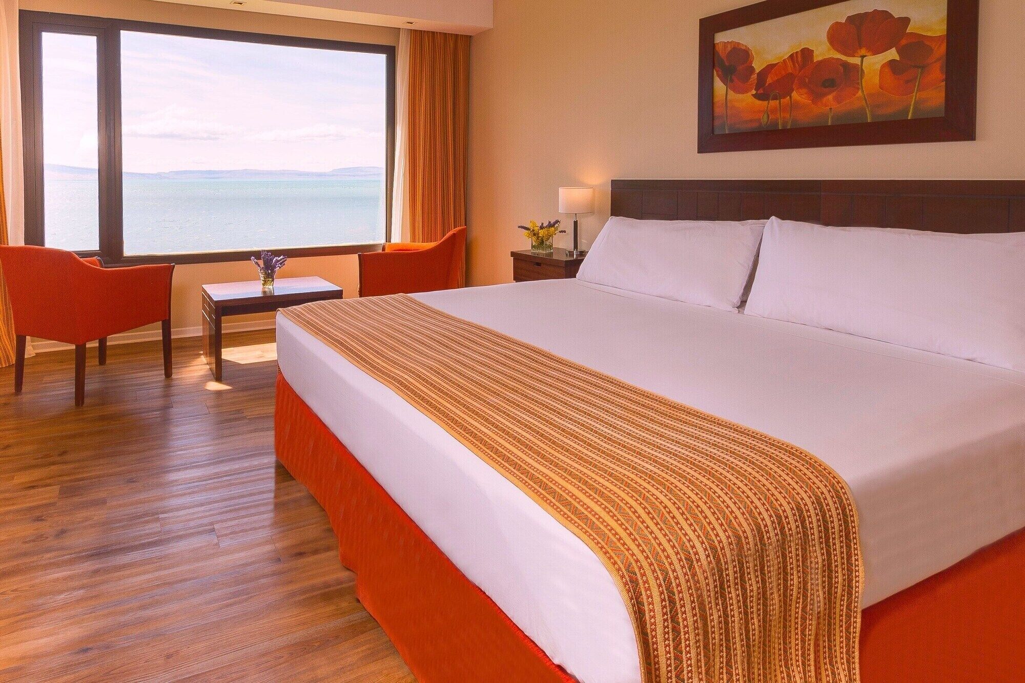 A hotel room with a large bed, a desk, a chair, and a view of the sea.