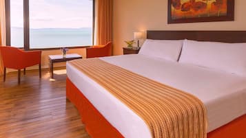 A hotel room with a large bed, a desk, a chair, and a view of the sea.