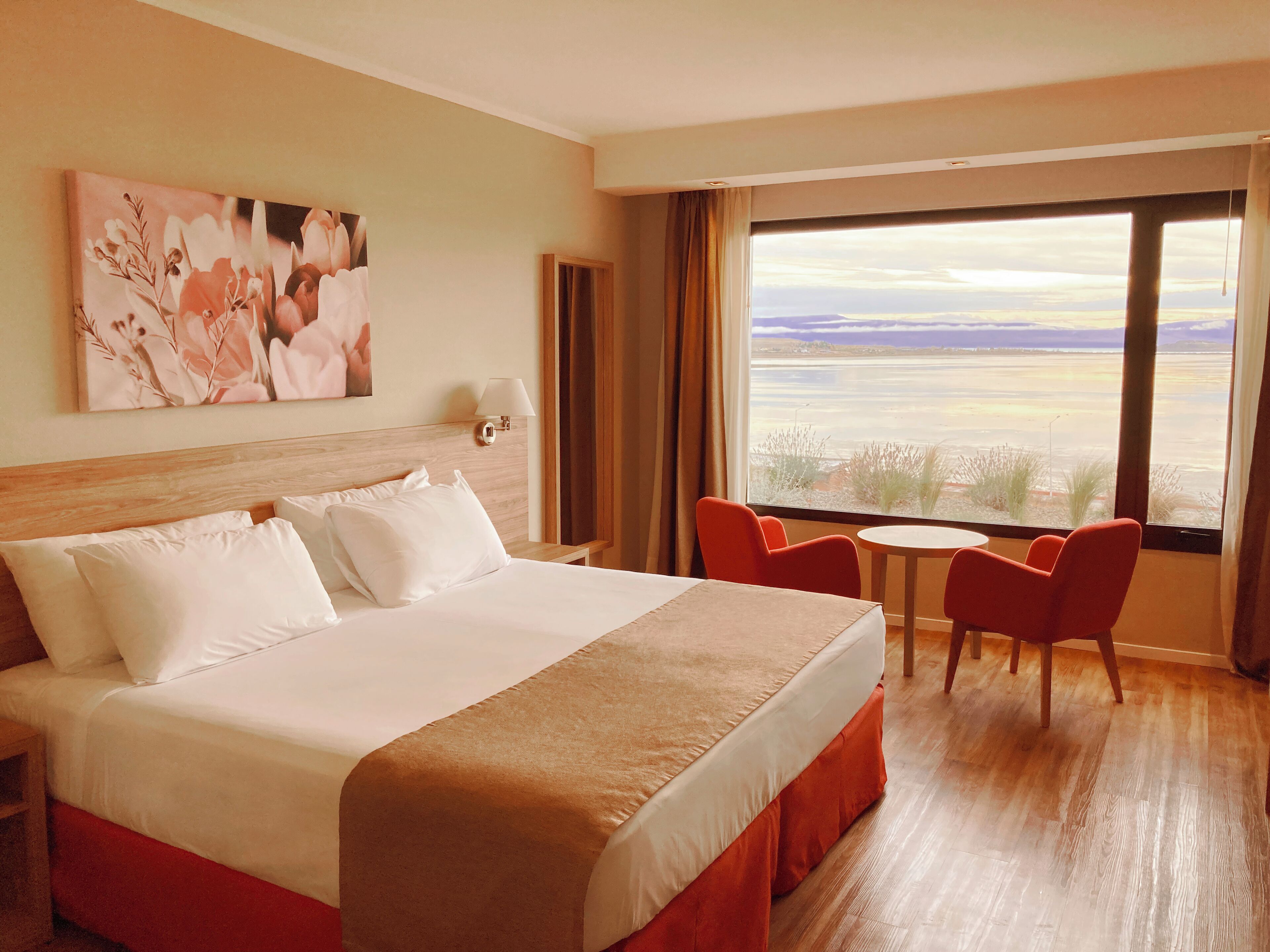 Ein Hotelzimmer mit einem großen Bett, einem Schreibtisch, zwei Stühlen und einem großen Fenster mit Blick.