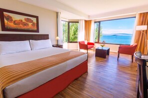 Ein Hotelzimmer mit einem großen Bett, einem Schreibtisch, einem Stuhl und Meerblick.