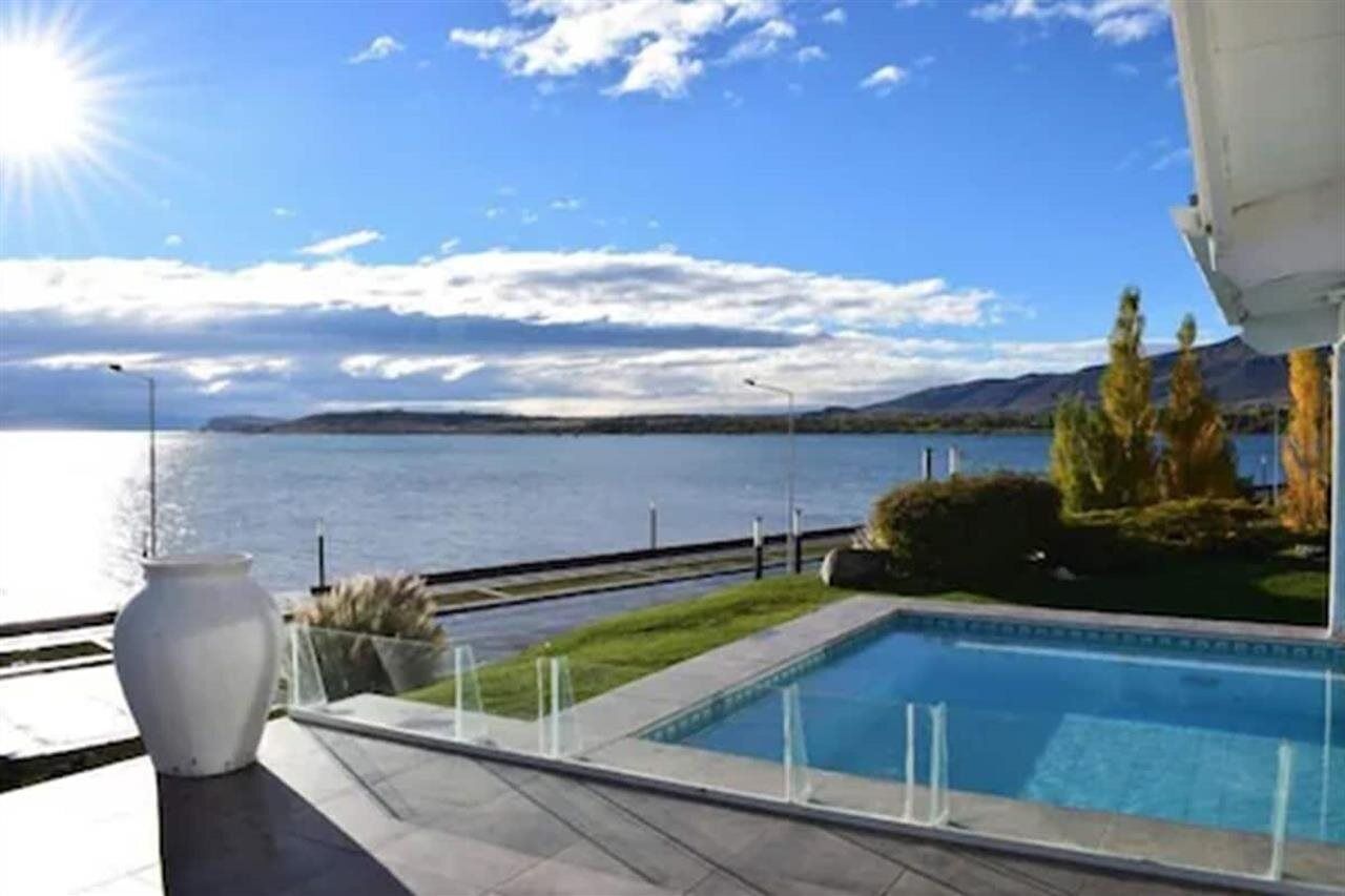 A pool with a view of a lake and mountains, a white vase, and a clear sky.