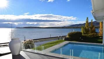 A pool with a view of a lake and mountains, a white vase, and a clear sky.