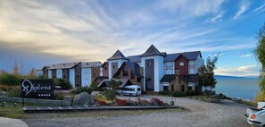A hotel with a signboard, multiple buildings with varying roof designs, and a body of water in the background. - Xelena Hotel and Suites (El Calafate)