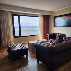 Ein Zimmer mit großem Fenster, einem Ledersofa, passendem Hocker und einem kleinen Tisch mit einem Glas.