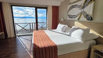 Une chambre d’hôtel avec un grand lit, une vue sur la mer et un tableau au mur.