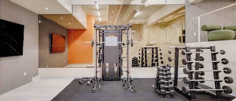 A gym with a squat rack, weight bench, and various dumbbells.