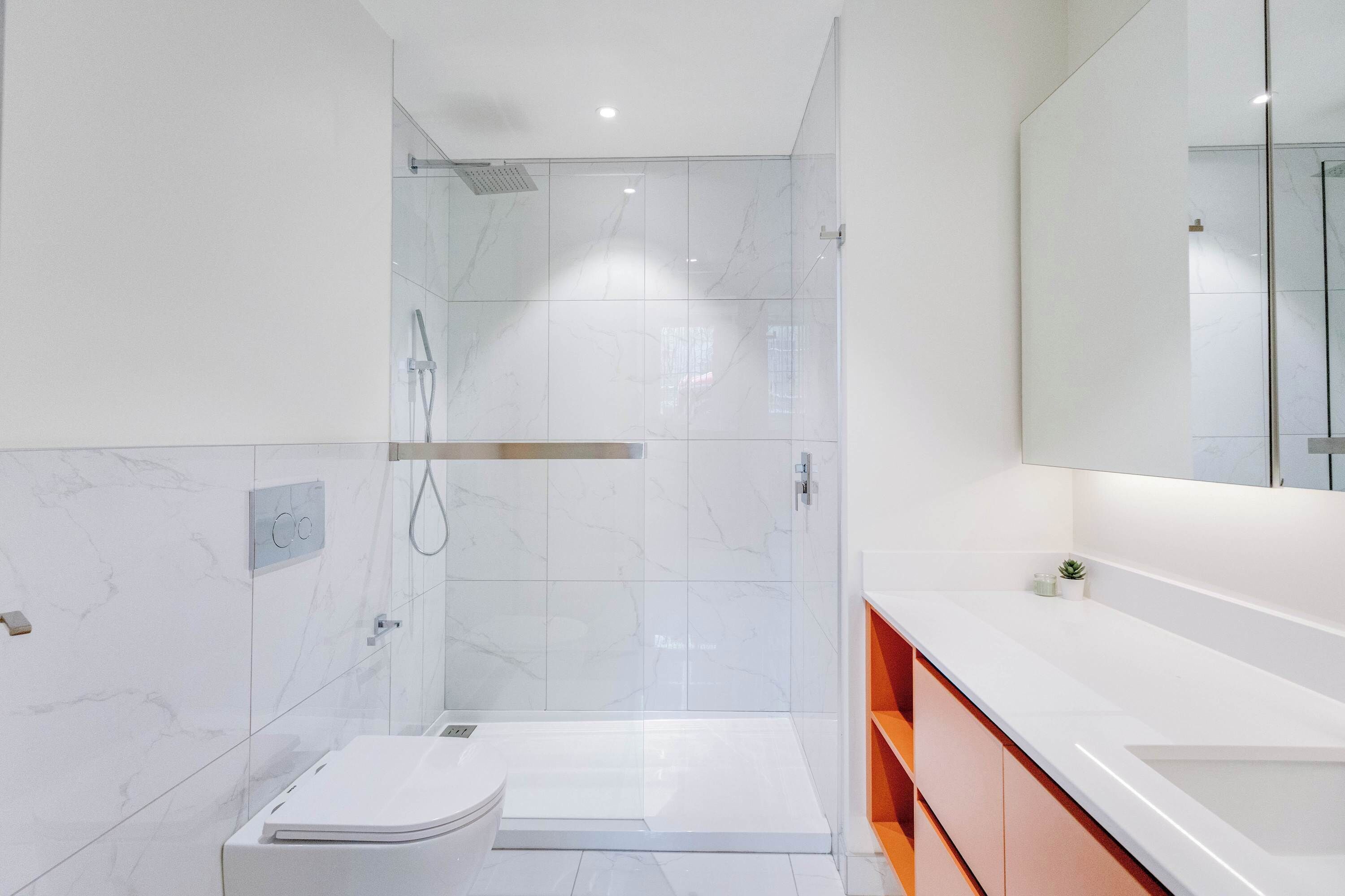 A modern bathroom with a glass-enclosed shower, a white toilet, and a large mirror above a white sink.