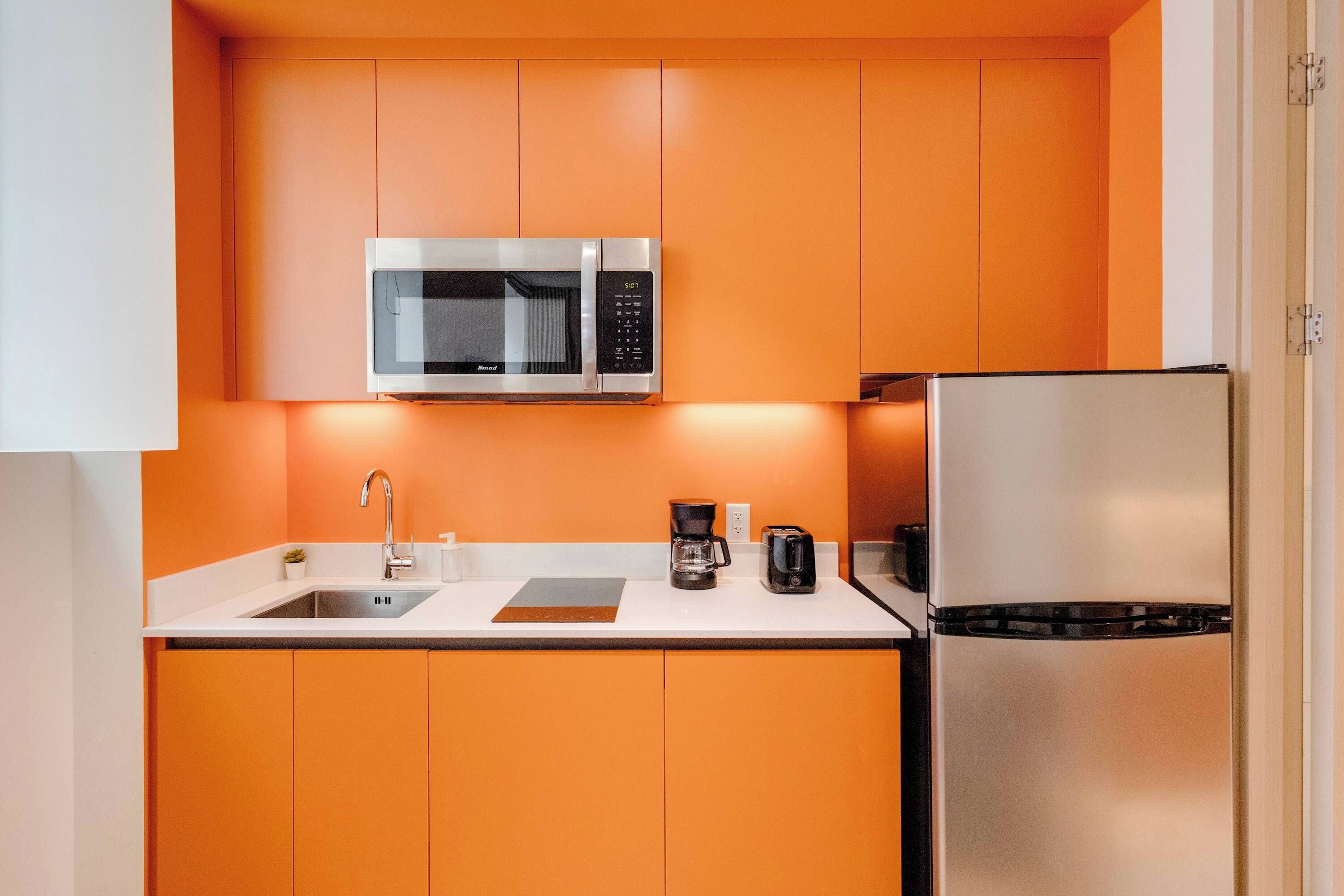 Cocina compacta con microondas, refrigerador, lavabo y cafetera.