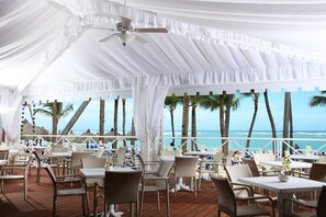 An outdoor dining area with tables and chairs, a ceiling fan, and a view of the ocean. - Bahia Principe Explore Esmeralda (Punta Cana)