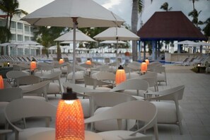 Buiten zitplaatsen met parasols en stoelen, een zwembad en een gebouw met een blauw dak.