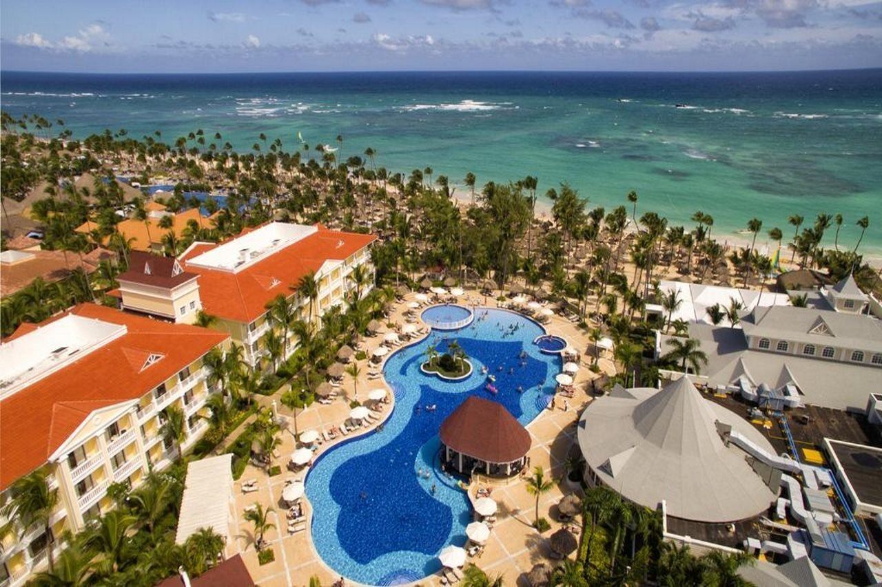 A resort with a large swimming pool, beachfront, and palm trees.