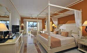 A four-poster bed with a canopy, a television, a desk with a lamp, and a view of the outdoors. - Bahia Principe Explore Esmeralda (Punta Cana)