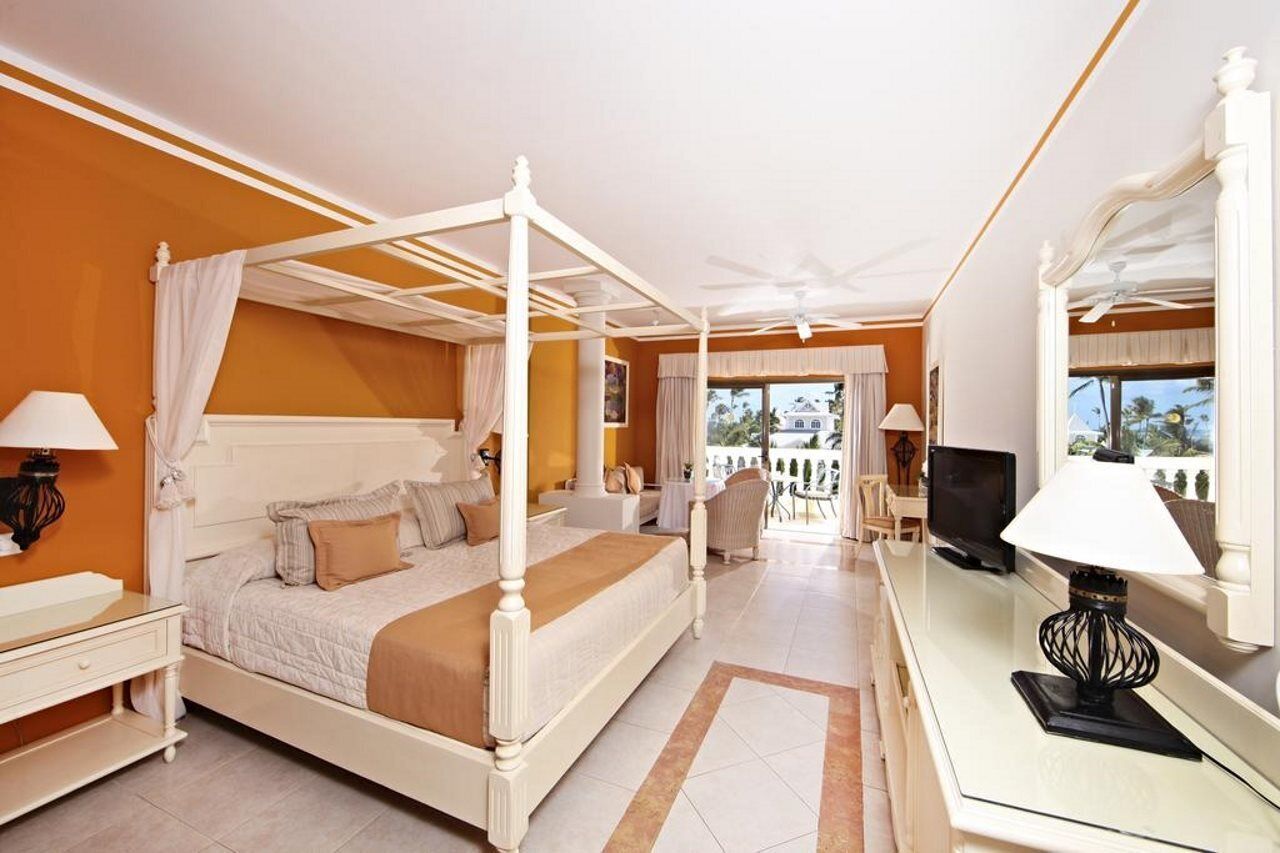 Un lit à baldaquin dans une chambre d’hôtel avec un balcon, une télévision et un bureau avec une lampe.