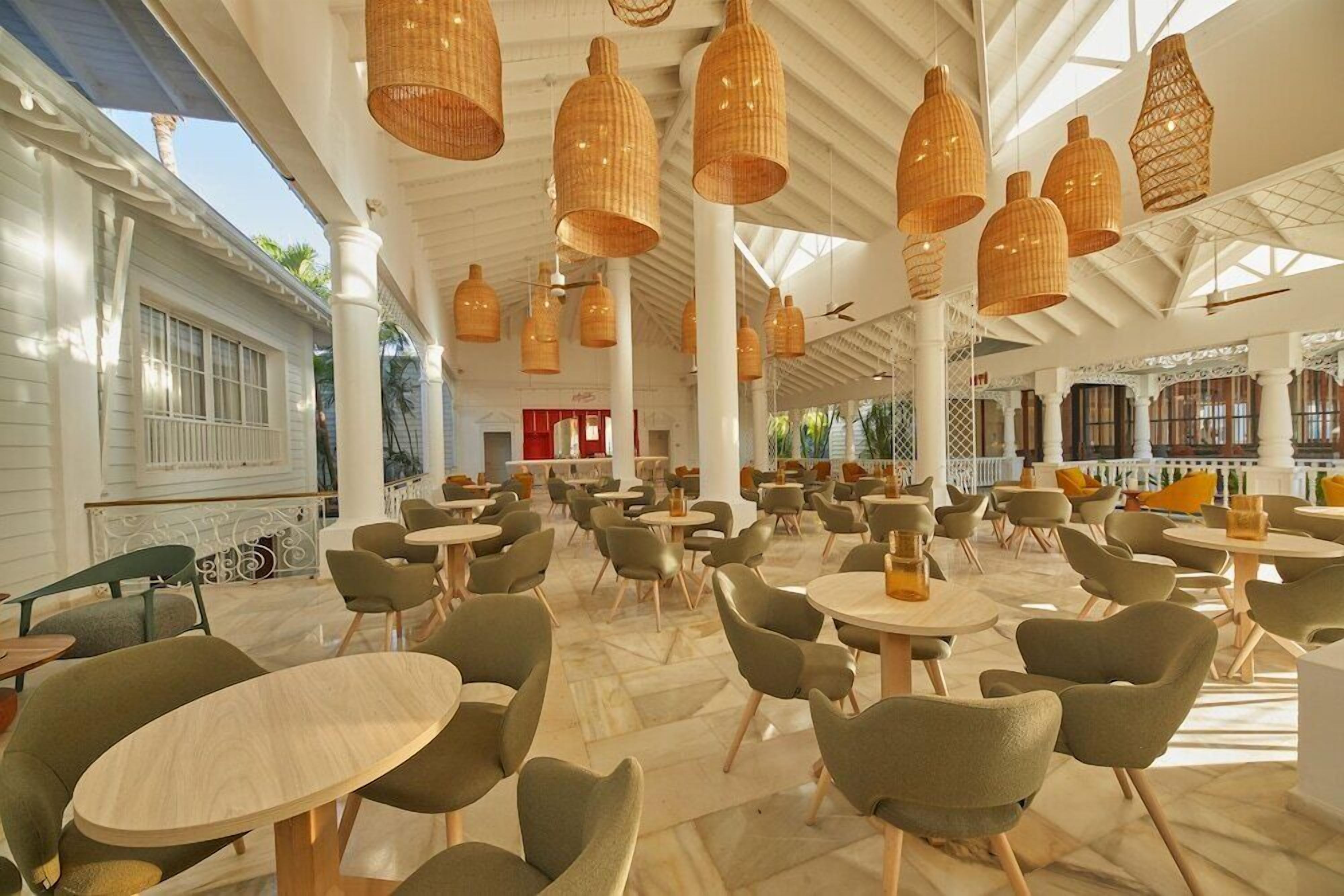Un vaste espace intérieur doté de plusieurs tables et chaises rondes, de grands luminaires suspendus en osier et d’un mur extérieur blanc.