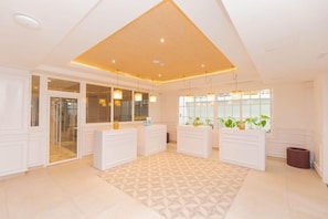 A hotel lobby with a reception desk, a patterned floor, and a large window with plants. - Bahia Principe Explore Esmeralda (Punta Cana)