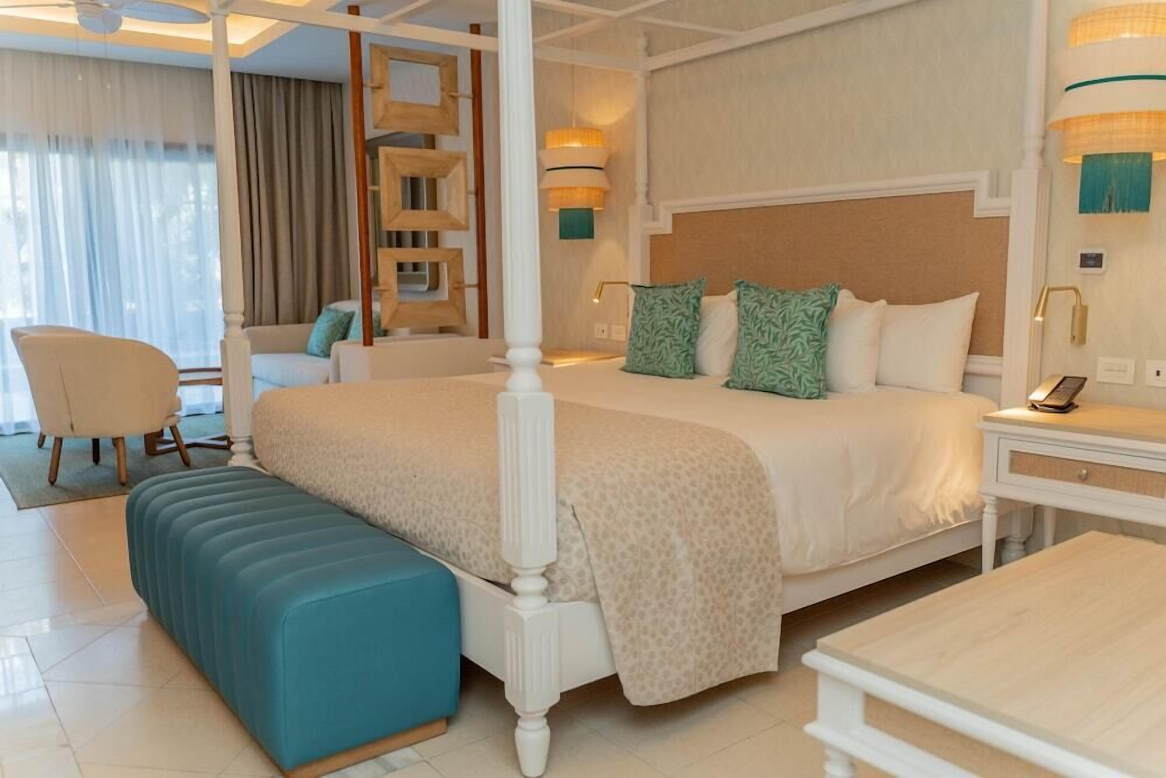 A four-poster bed with a headboard, a bedside table with a lamp, and a bench.