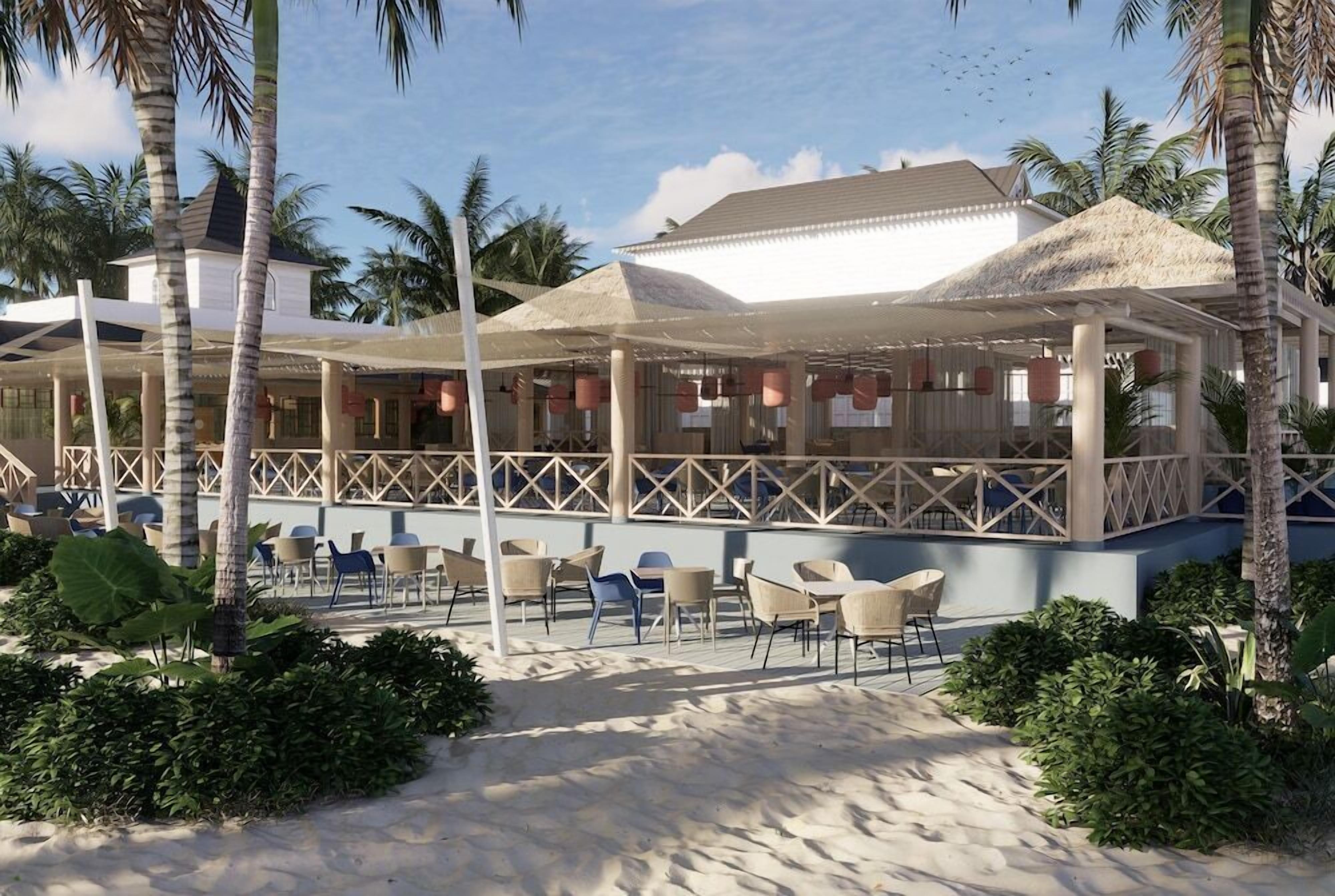 Un restaurant situé en bord de mer, avec une terrasse, des palmiers et un espace abrité.