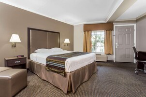 Habitación de hotel con cama, lámparas de noche, escritorio, silla y ventana con cortinas.