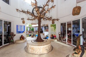 Zona de recepción con una escultura arbórea central, una lámpara colgante de mimbre y un cartel que indica la recepción.