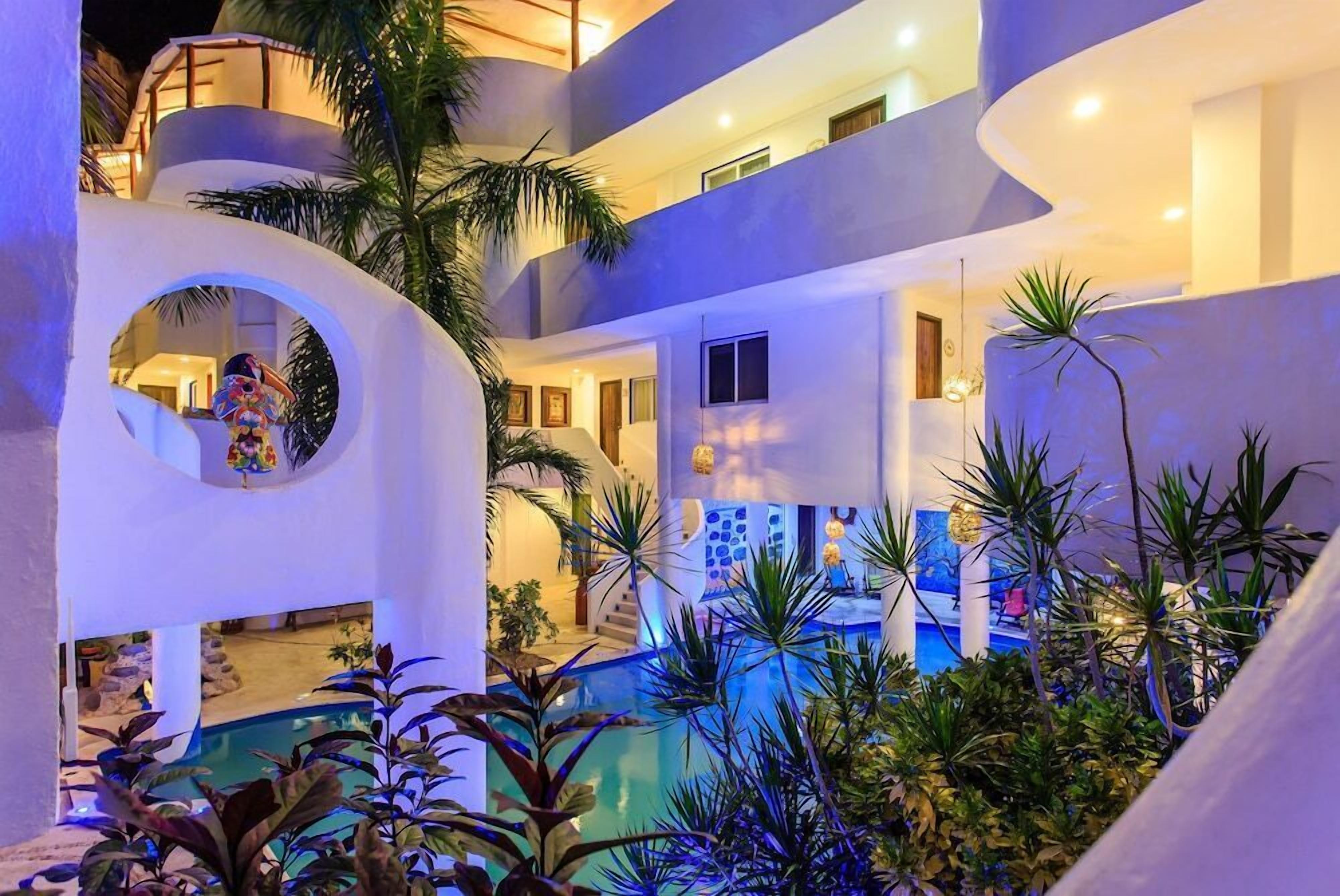 Un hotel de varios niveles con una zona de piscina rodeada de plantas tropicales.