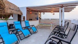 Eine Dachterrasse mit Liegestühlen, einem Tisch und einer Struktur mit Reetdach.
