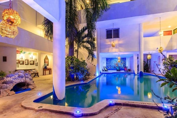 A pool area with a stone edge, palm trees, and a mural. - Matan Kaan by Guruhotel (Mahahual)