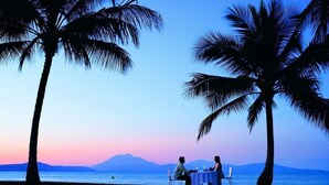 Un couple est assis à une table, devant un panorama sur la mer et les montagnes.