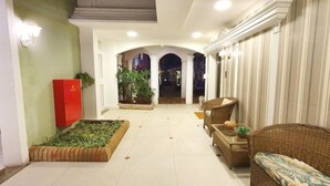Um saguão de hotel com balcão de recepção, área de estar e um canto com plantas.