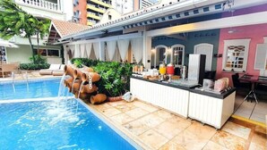 Uma área à beira da piscina com bar, assentos e uma piscina com atração aquática.