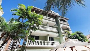 Um hotel com várias andares, varandas, palmeiras e área de estar externa.