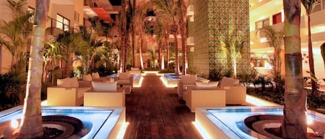 A hotel courtyard with a wooden walkway, palm trees, and outdoor seating areas.