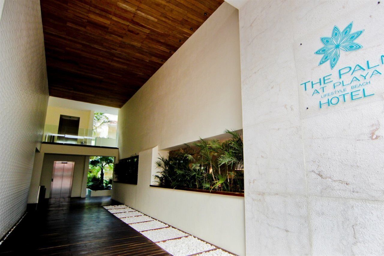 A hallway with a wooden ceiling, a white wall with a logo, and a plant wall.