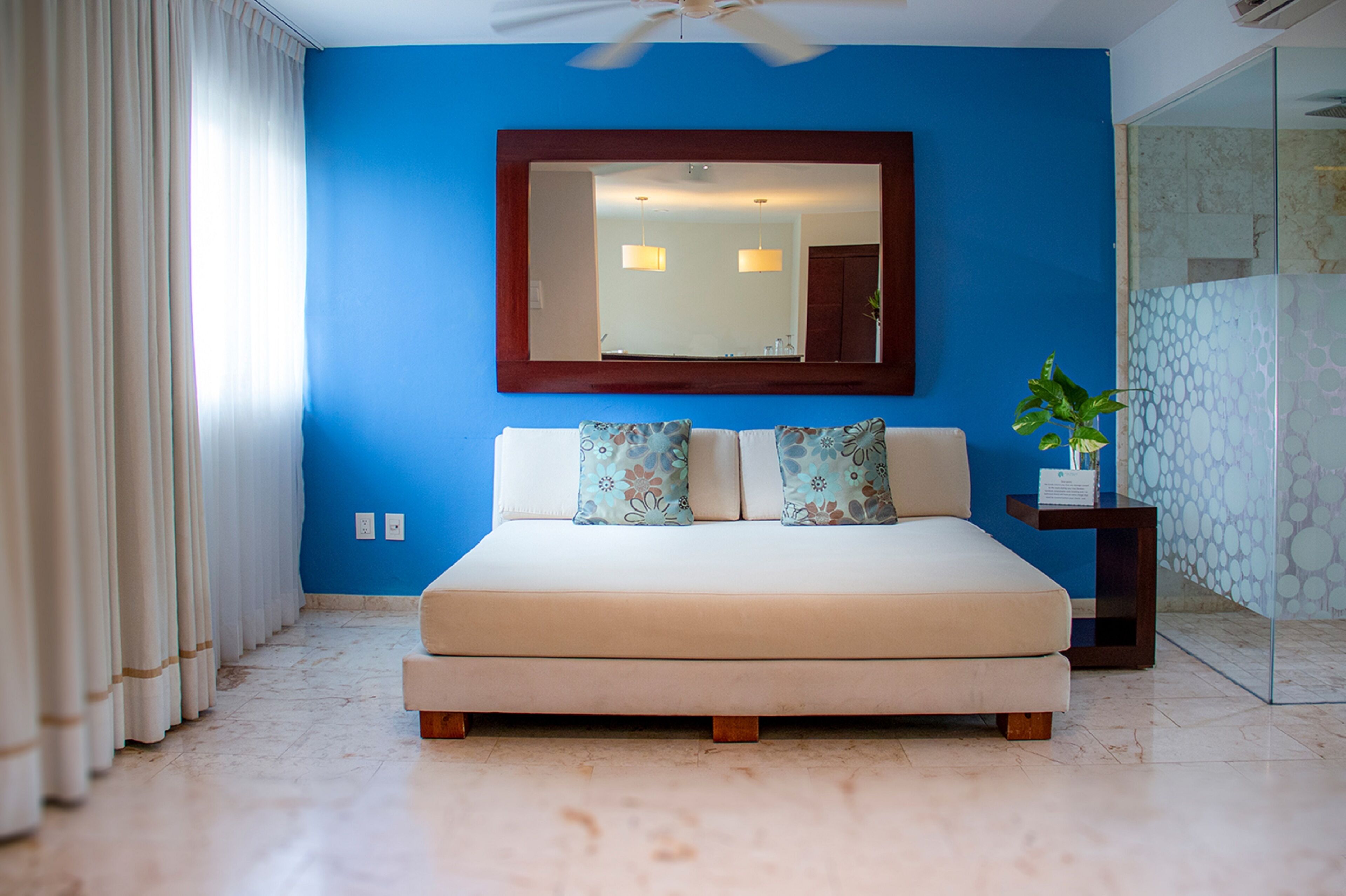 Une chambre avec un grand lit, un ventilateur de plafond, un miroir et une plante en pot.