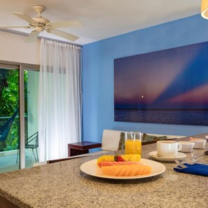 A breakfast setup with a plate of fruit, a glass of orange juice, and a cup on a granite countertop. - The Palm at Playa (Playa del Carmen)