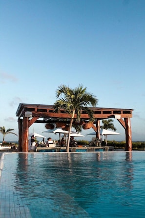 A pool area with a wooden pergola, palm trees, and umbrellas. - The Palm at Playa (Playa del Carmen)