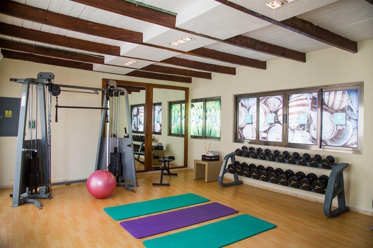 Un gimnasio con equipo de ejercicio, colchonetas y mancuernas.