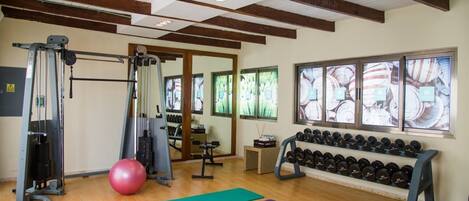 Un gimnasio con equipo de ejercicio, colchonetas y mancuernas.