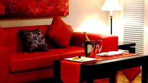 Un divano rosso con un cuscino decorativo, un tavolo con una bottiglia e dei bicchieri, e una lampada in una stanza con una finestra.