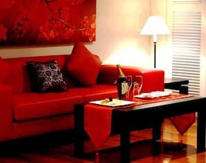Ein rotes Sofa mit einem dekorativen Kissen, ein Tisch mit Flasche und Gläsern sowie eine Lampe in einem Zimmer mit einem Fenster.