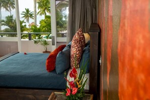 A bedroom with a bed, pillows, a vase with flowers, and a view of palm trees and a waterfall through the window. - The Pearl Resort Spa & Golf Course (Pacific Harbour)